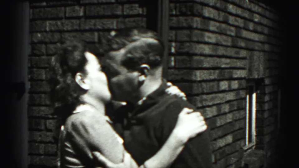 An adult woman and man embrace and kiss near the brick exterior in the 1946 New Cumberland home-movie clip.