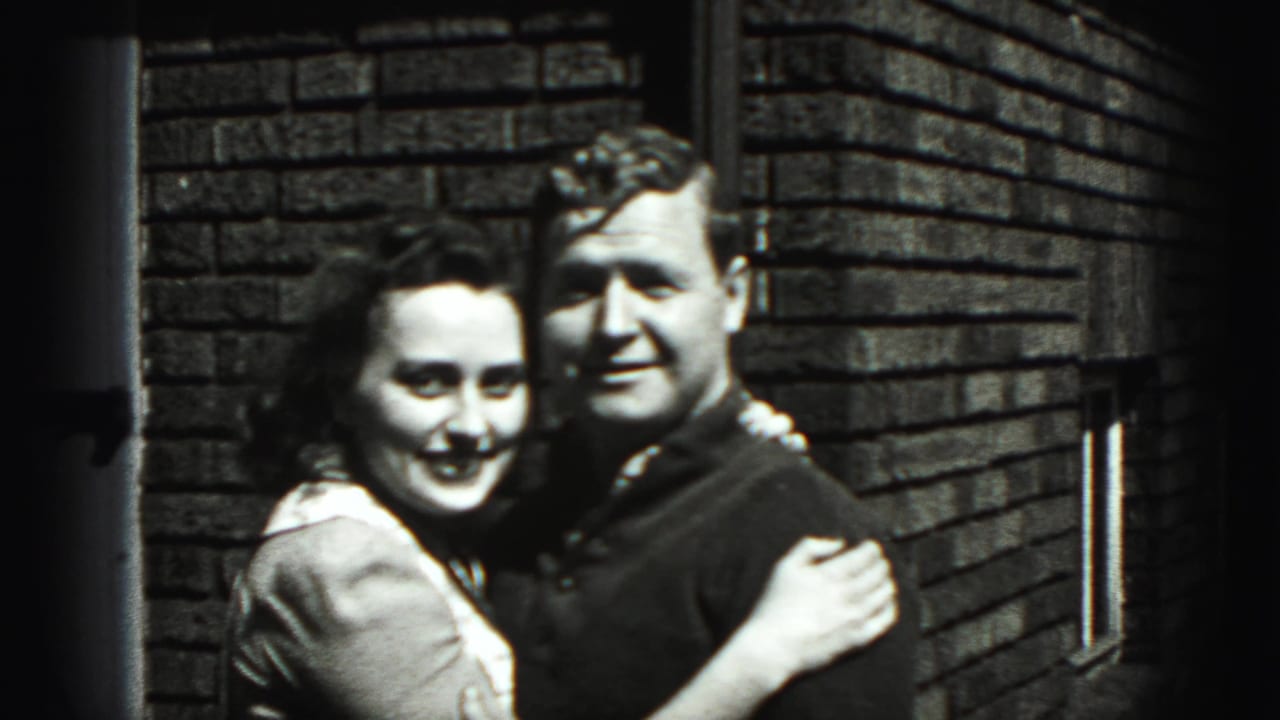 Smiling couple holding each other in front of a brick wall.