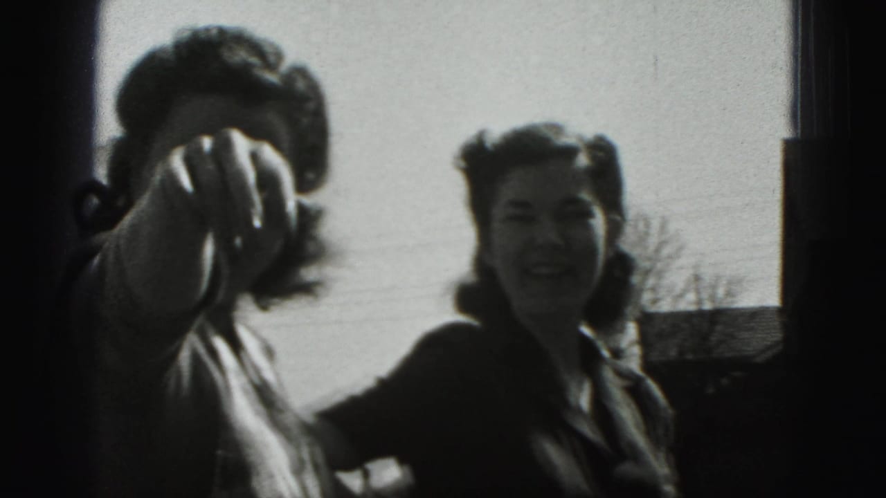 Two young women outdoors, one reaching or pointing toward the camera while the other smiles.
