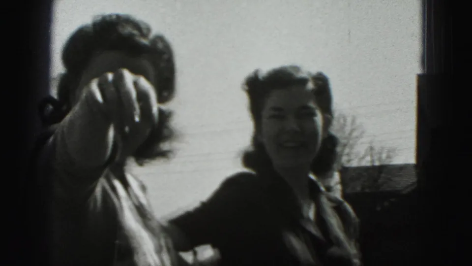In 1946 New Cumberland, two young women stand outside in bright sun, with one playfully extending a hand toward the lens.