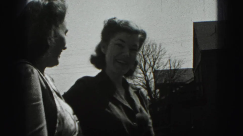 Two young women in 1940s clothing stand outdoors in New Cumberland, with one in profile and the other smiling at the camera.