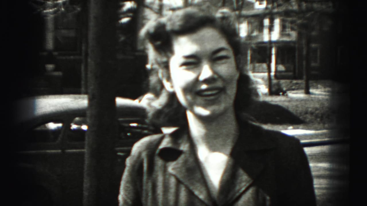 Smiling woman framed closer on a residential street with houses and a car behind her.