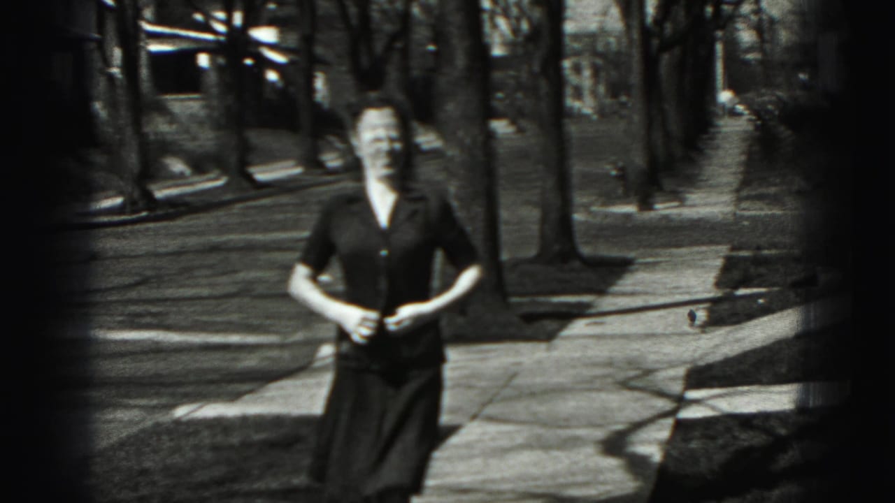 The young woman faces the camera and appears to button or adjust her blouse during the 1946 home-movie sidewalk shot.