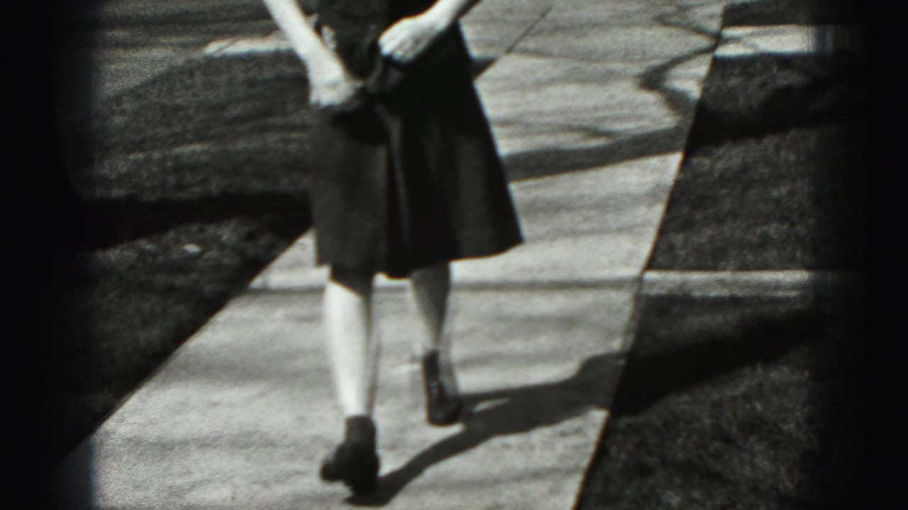 The frame crops the woman from upper body to legs as she walks on the residential sidewalk, with lawn and curb visible.