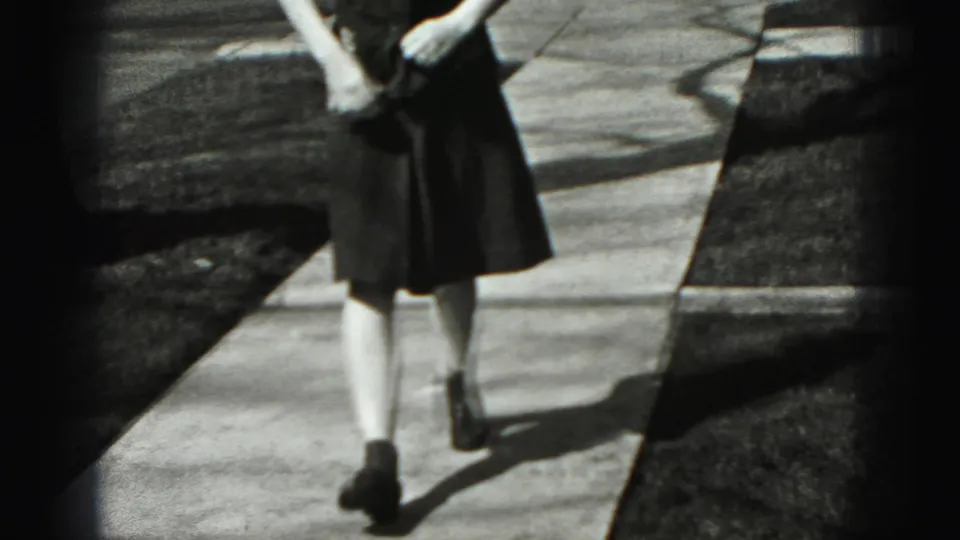 The frame crops the woman from upper body to legs as she walks on the residential sidewalk, with lawn and curb visible.