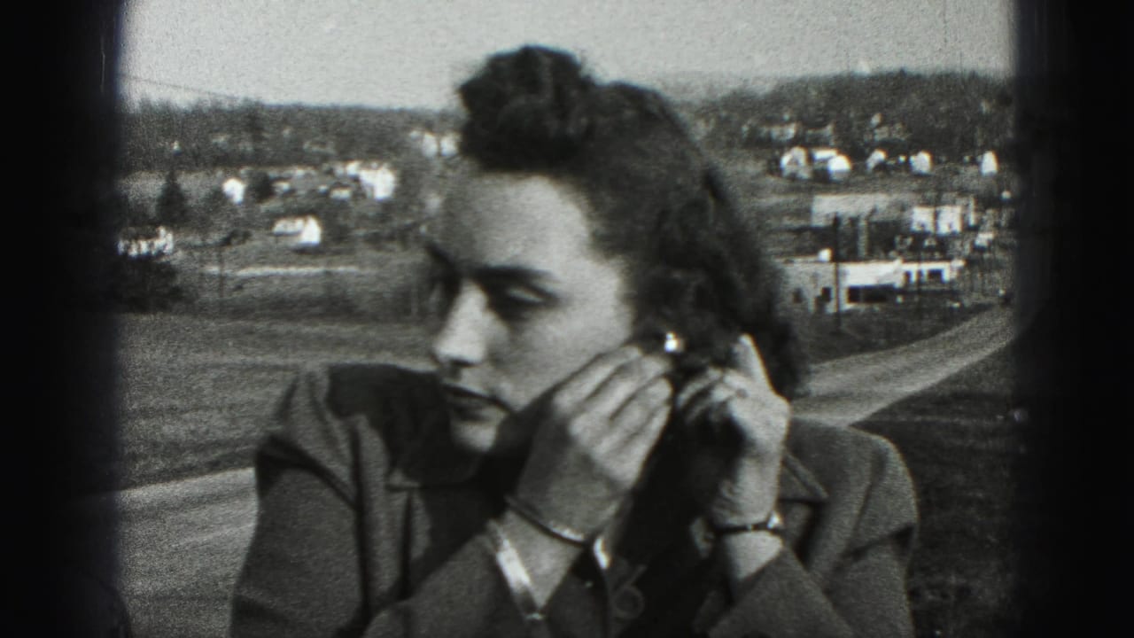 A close 8mm frame shows the woman adjusting an earring, with bracelets visible and a New Cumberland hillside settlement in the background.