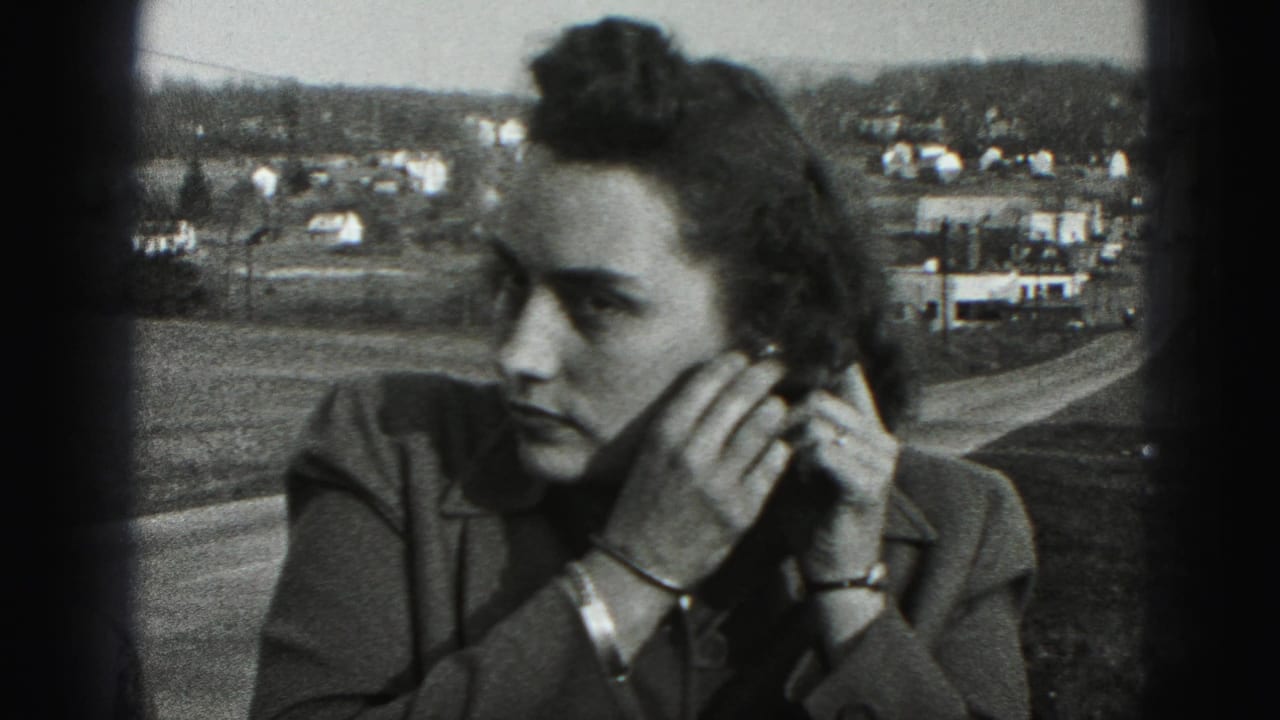 The woman looks aside while adjusting her earring, framed close against roads, houses, and low hills in 1946 Pennsylvania footage.