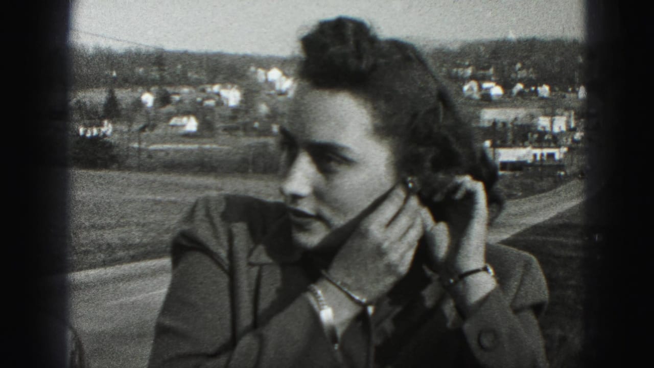 The woman appears in profile while adjusting her left earring, with New Cumberland town buildings and open ground behind her.