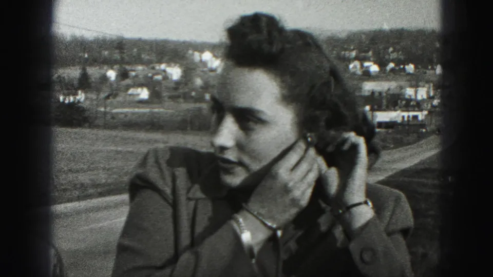 The woman appears in profile while adjusting her left earring, with New Cumberland town buildings and open ground behind her.