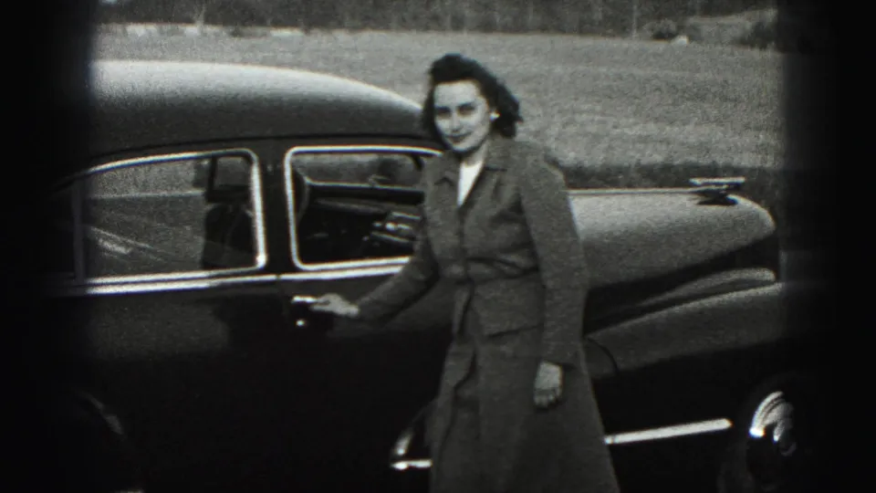 In 1946 New Cumberland home-movie footage, a woman smiles toward the camera while standing beside a dark mid-century sedan.