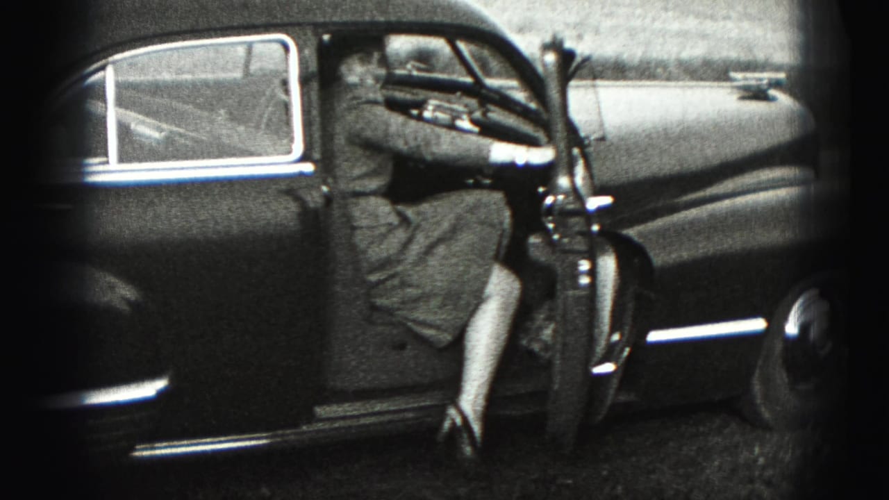 A woman in a dress steps into the driver's side of a dark 1940s sedan in New Cumberland.
