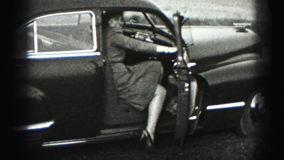 A woman in a dress steps into the driver's side of a dark 1940s sedan in New Cumberland.