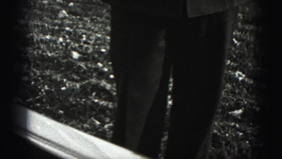 A home-movie view shows a standing figure's lower legs beyond a bright sill or frame edge in the outdoor New Cumberland setting.