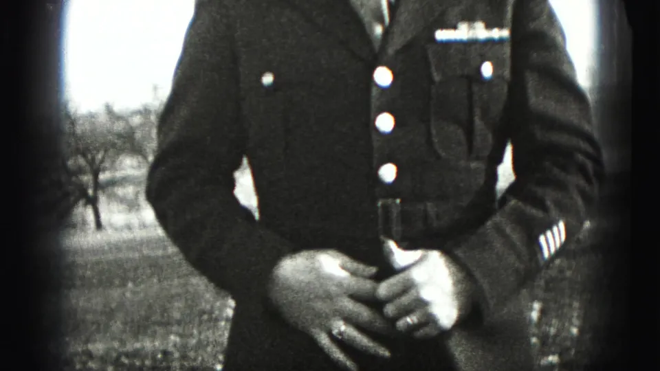 A uniformed soldier in the 1946 New Cumberland home movie stands outdoors with hands clasped, jacket buttons and sleeve stripes visible.