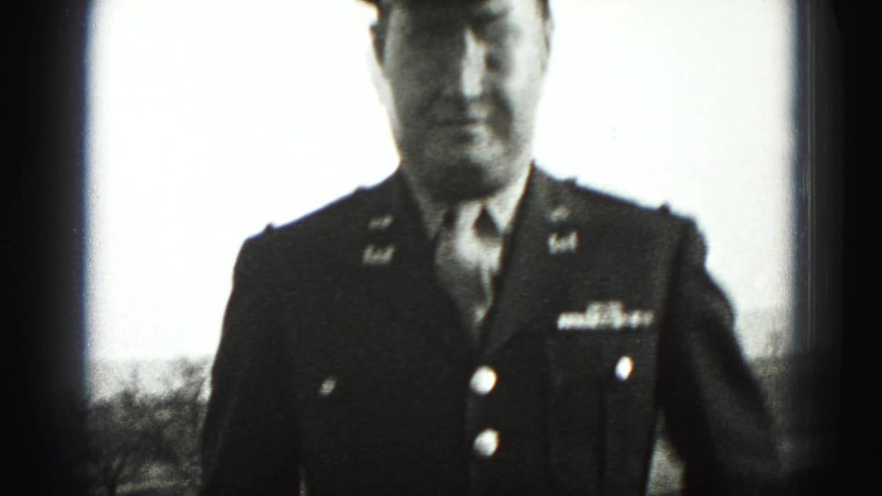 Uniformed man stands close to the camera with cap and jacket insignia visible.