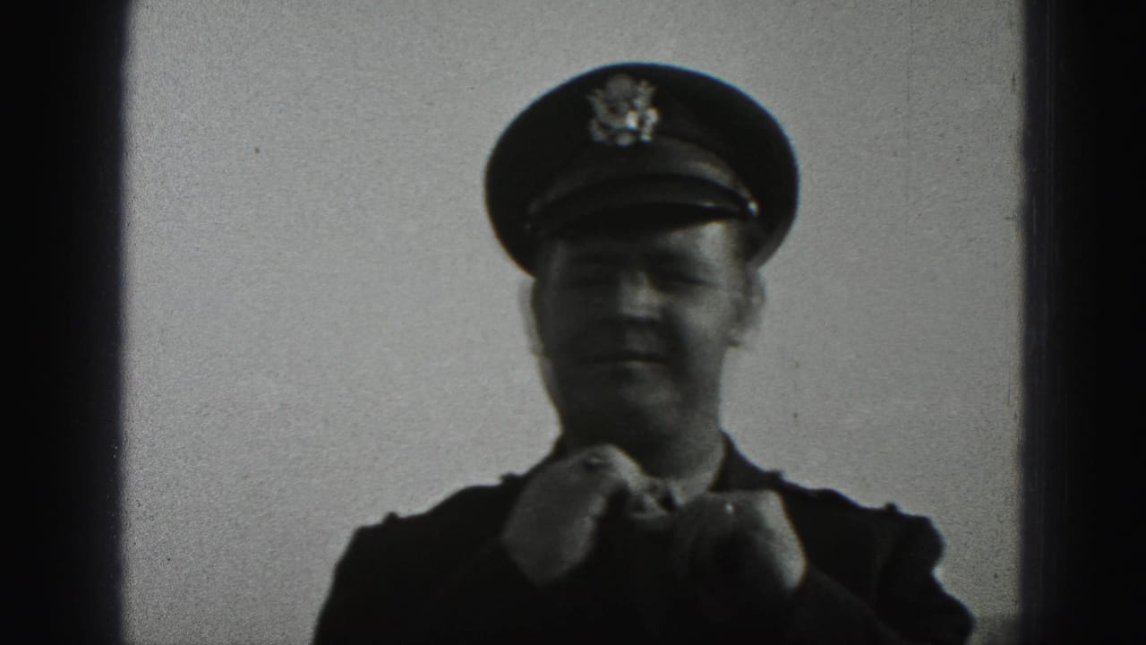 Uniformed man adjusts his tie beneath a peaked cap against a plain sky.