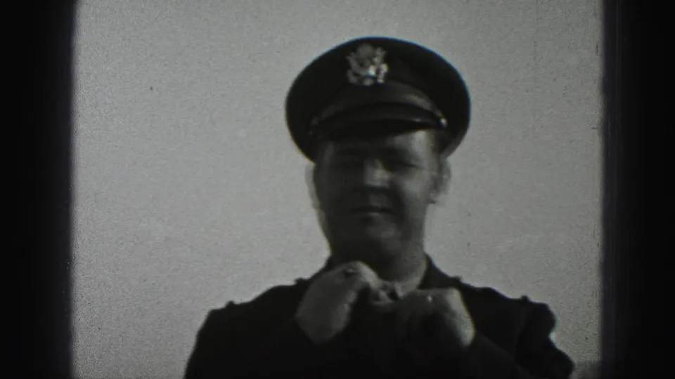 The man in a military-style uniform adjusts his tie outdoors, with his peaked cap and jacket shoulders visible against the sky.