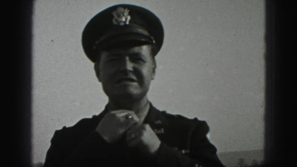 In the New Cumberland outdoor scene, the uniformed man holds his tie with both hands, cap brim shading his face.