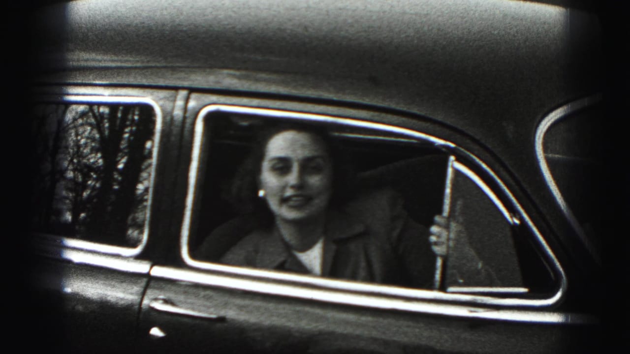 A woman seated inside a mid-century car faces the camera through the side window in New Cumberland home-movie footage.