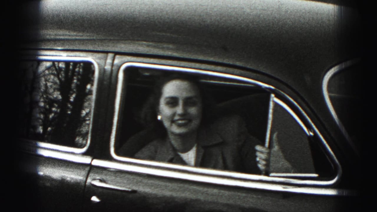 A black-and-white 8mm frame shows the young woman leaning at the rear window, with chrome trim and reflected trees around her.