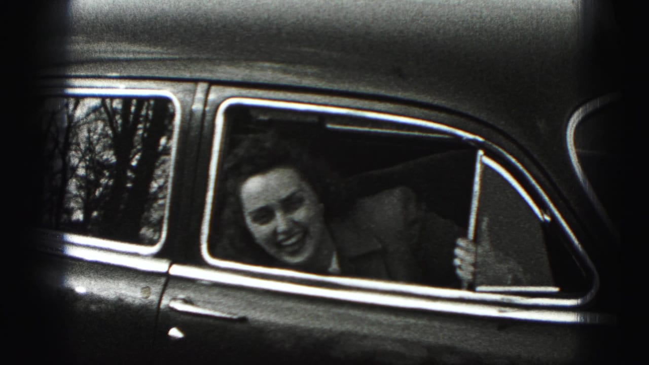 Woman smiling from the rear window of a vintage car.
