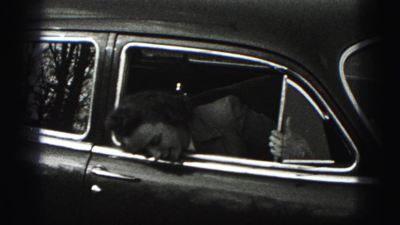 Woman leaning down inside the rear window of a vintage car.