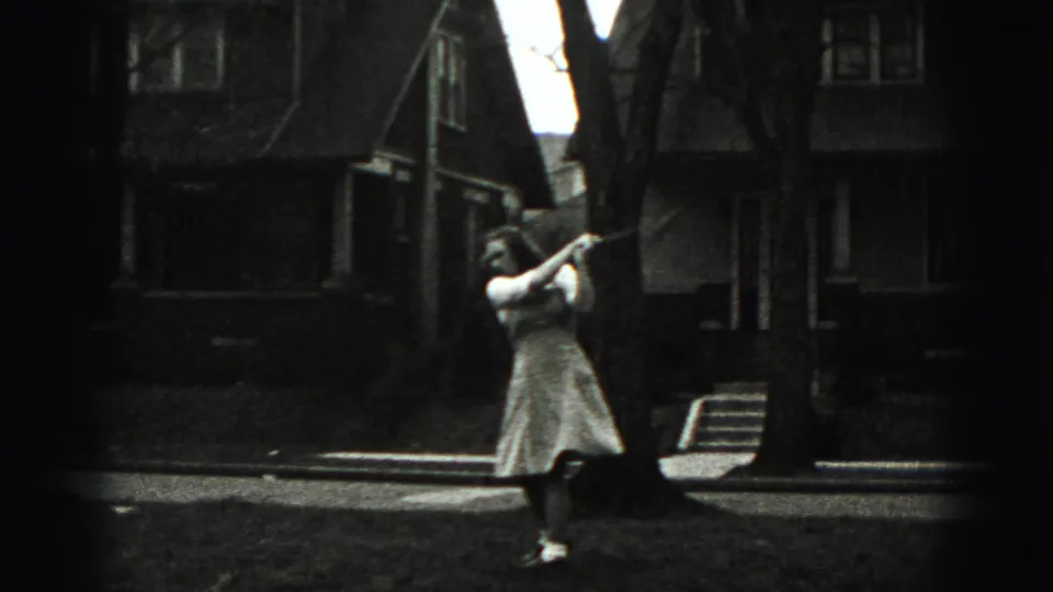 In the residential New Cumberland scene, a woman in a light dress holds a golf club on a lawn near houses and bare trees.