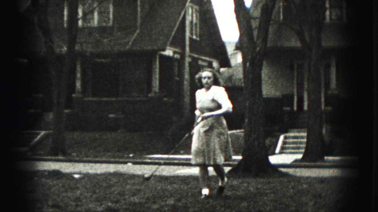 A woman in a light dress walks across a residential lawn with a golf club, framed by houses and tree trunks.