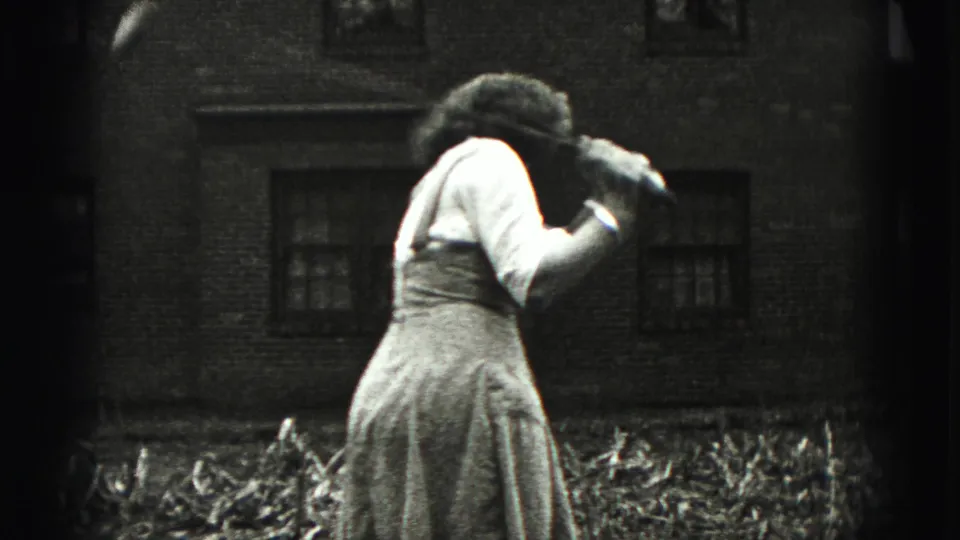 The woman leans forward during the golf practice scene, filmed close to a brick residential wall in 1946 home-movie footage.