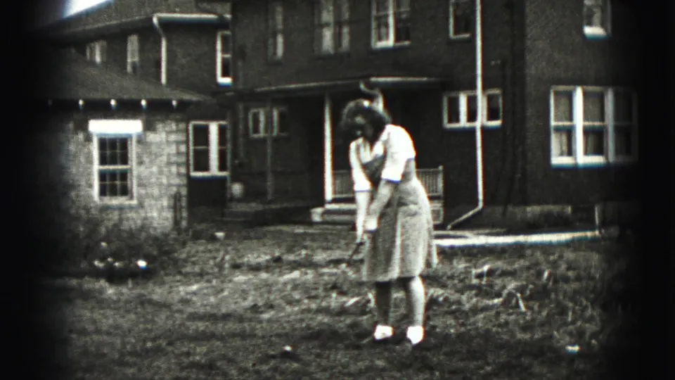 A woman practices a golf swing in the yard of a New Cumberland residence, with house windows and bare ground visible around her.