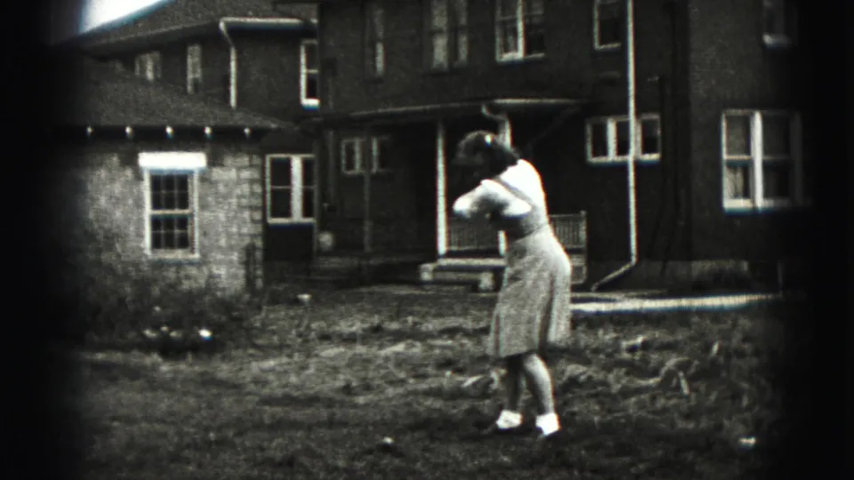 A woman swings a golf club in a New Cumberland backyard, with house windows and porch details behind her.