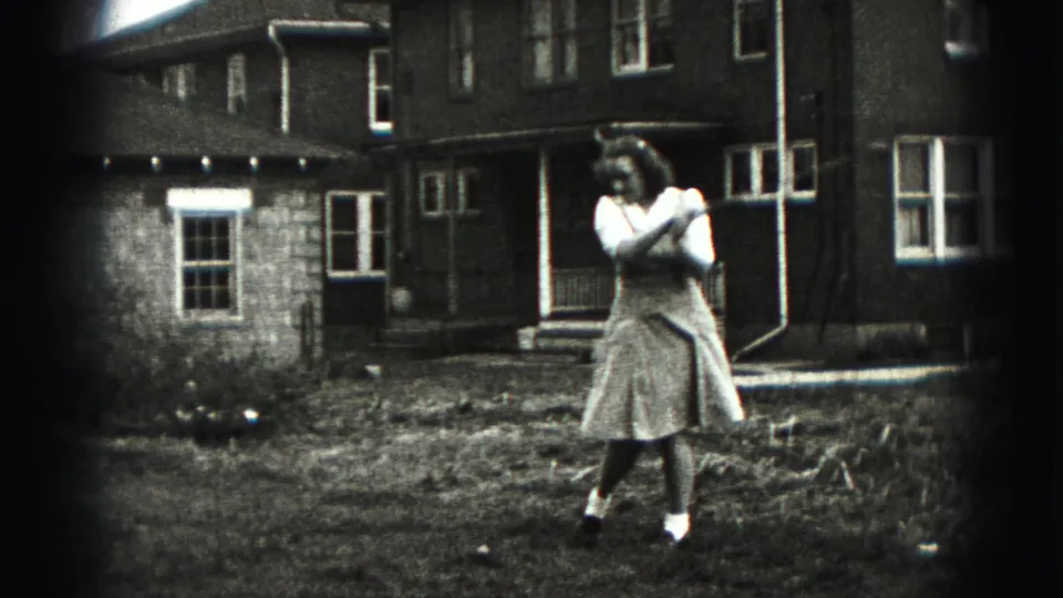 A woman in a skirt stands with her arms near her shoulder after a golf swing in a 1946 backyard scene.