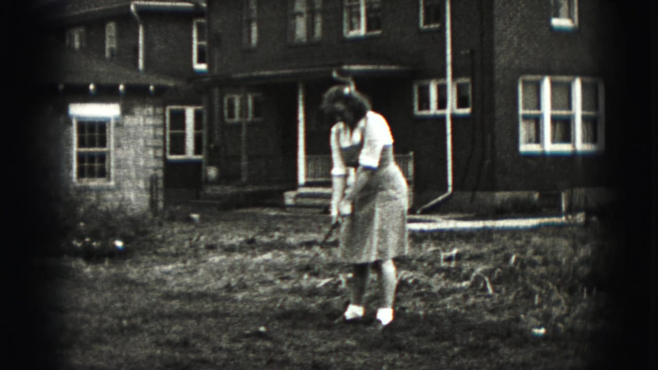Woman bends over a golf club in the yard with a house exterior behind her.
