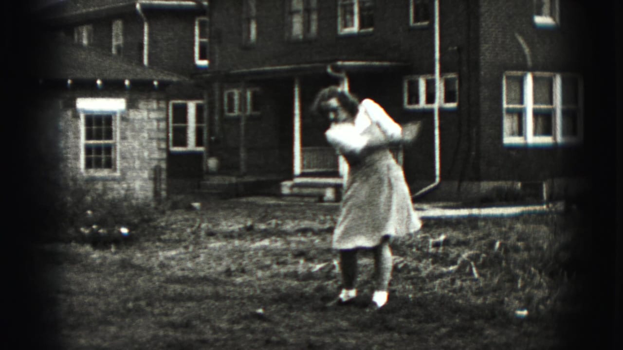 The woman completes an energetic golf follow-through in a residential backyard, with brick walls, windows, and porch steps visible.