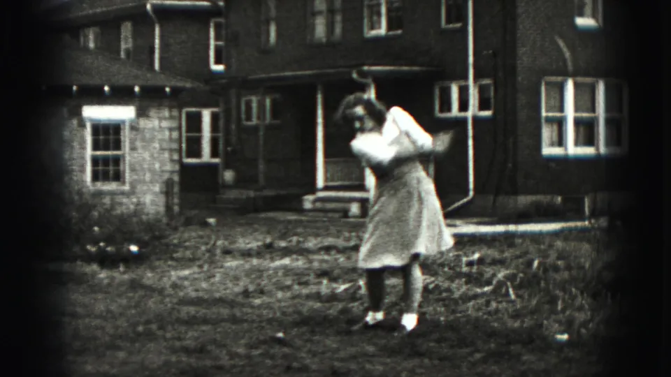 The woman completes an energetic golf follow-through in a residential backyard, with brick walls, windows, and porch steps visible.