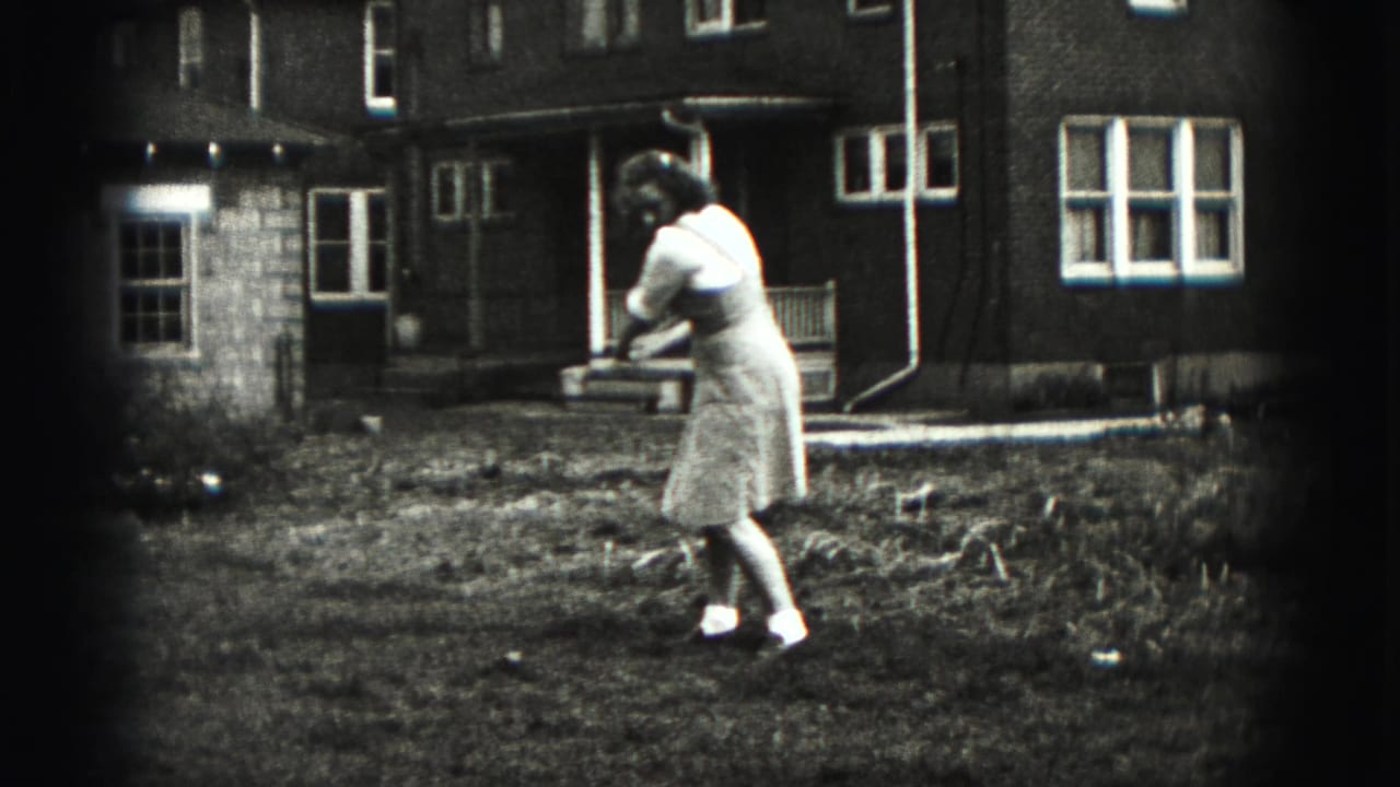 The woman follows through on a casual golf swing in a grassy New Cumberland backyard, filmed on black-and-white 8mm.