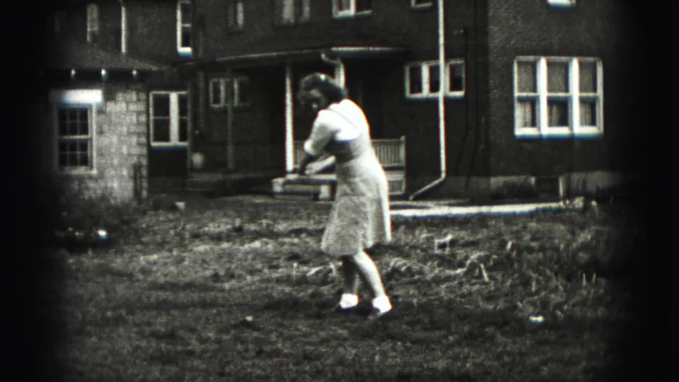 The woman follows through on a casual golf swing in a grassy New Cumberland backyard, filmed on black-and-white 8mm.