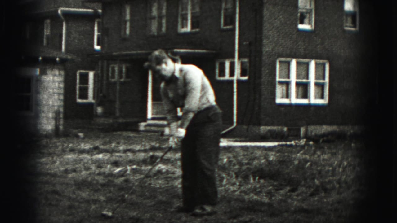 A man in a light shirt and dark trousers takes his turn with the golf club in the New Cumberland backyard.