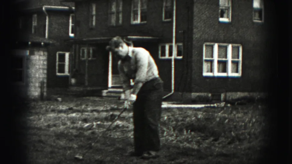 A man in a light shirt and dark trousers takes his turn with the golf club in the New Cumberland backyard.