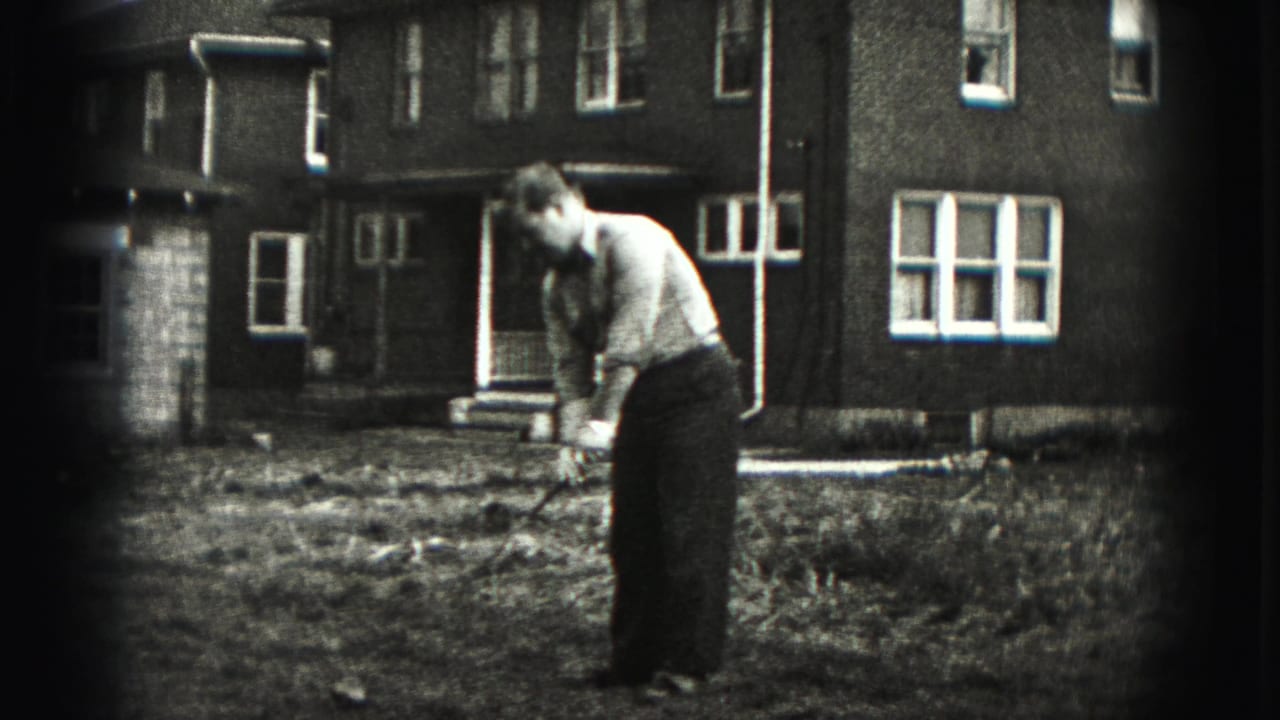 Man stands over a golf club in the yard with the house behind him.