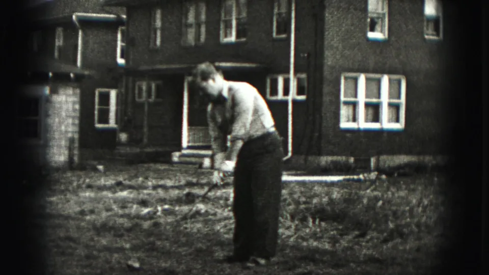 In the backyard scene, the man remains bent at address with the club near the ground before the brick house.