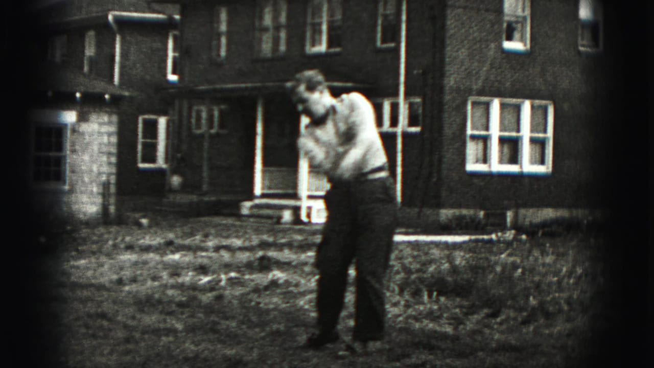 The man completes a golf swing follow-through in the yard, with the 1946 residential setting visible behind him.