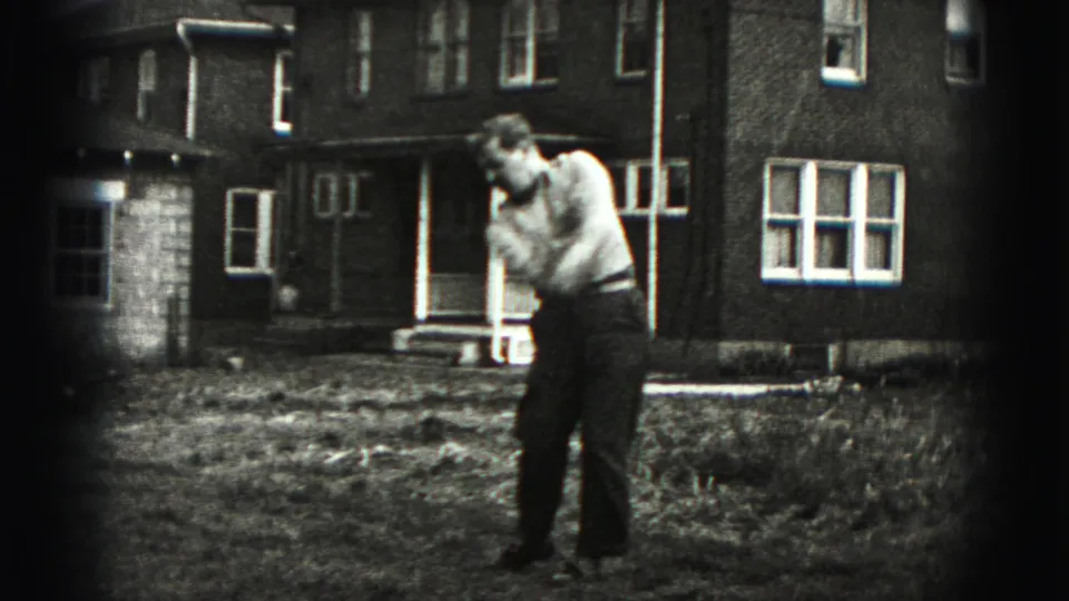 The man completes a golf swing follow-through in the yard, with the 1946 residential setting visible behind him.