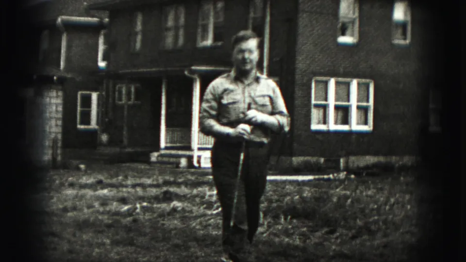 The man stands closer to the camera with his golf club in hand, framed by a grassy yard and brick residential exterior.