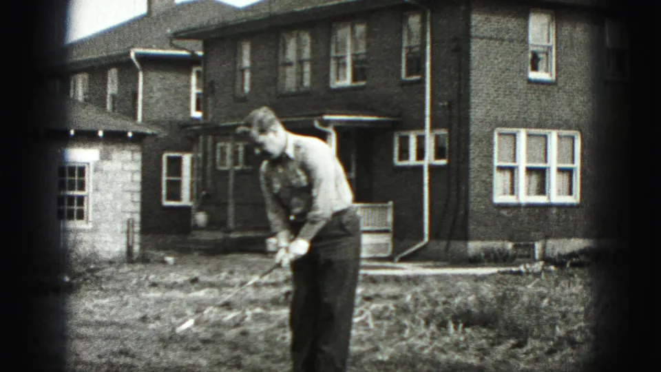 A man practices a golf swing in the front yard of a brick home in New Cumberland, Pennsylvania, in 1946 footage.