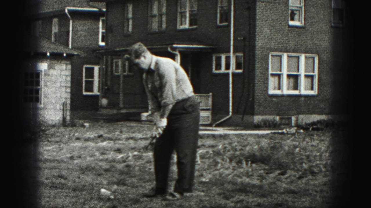 Man addresses a golf ball in a grassy yard outside a brick house.