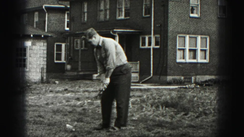 In 1946 New Cumberland home-movie footage, a man sets up a golf shot in a grassy yard before a brick residential building.