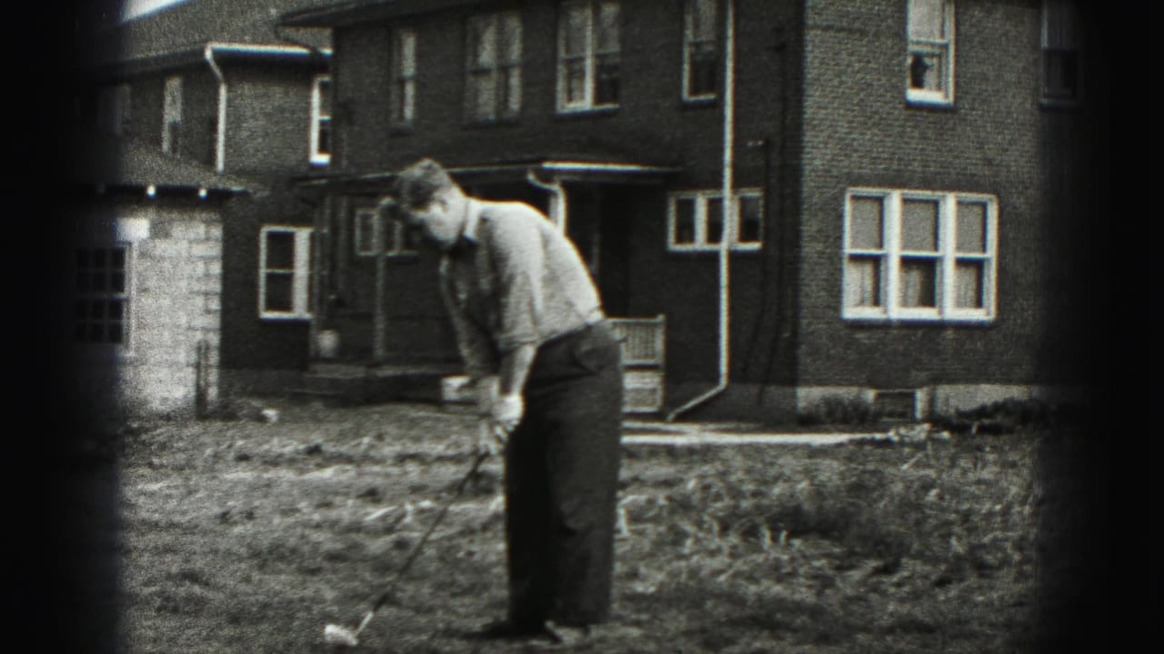 The man remains focused over the ball with a golf club in a New Cumberland yard, framed by brick walls and windows.