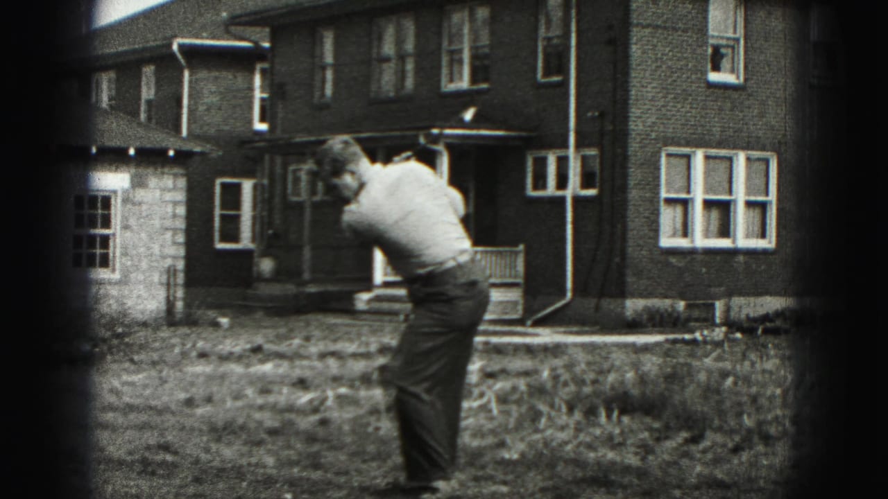The man follows through on a backyard golf swing in 1946 home-movie footage, with a brick house behind him.