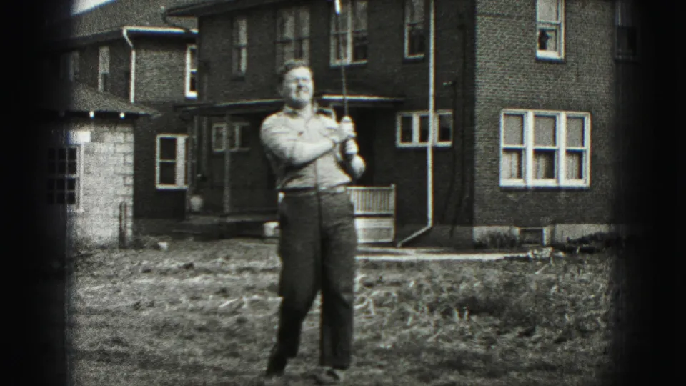After the swing, the man faces the camera and smiles while holding the golf club in the New Cumberland yard.